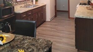 Una cocina compacta con refrigerador, microondas y lavamanos. Hay una mesa de comedor con una silla y un florero con flores.