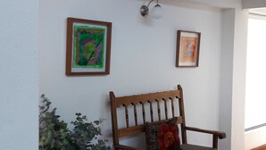 Ein Zimmer mit einer hölzernen Sitzbank, zwei gerahmten Kunstwerken, einer Topfpflanze und einem Fliesenboden.