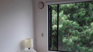 Ein Schlafzimmer mit zwei Betten, einem Fenster mit Blick auf Bäume, einer Lampe und einer Steckdose.
