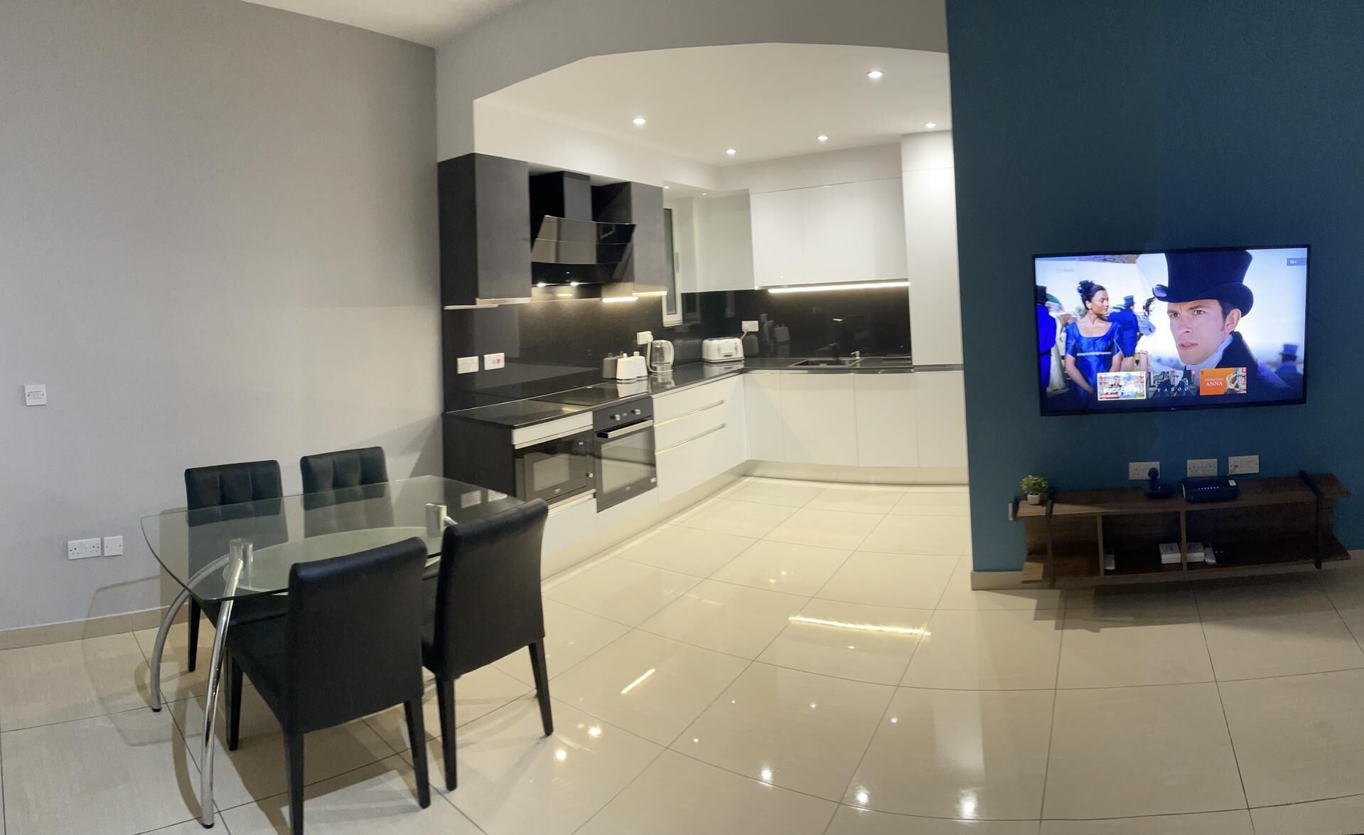 Cocina moderna con comedor, televisor de pantalla plana en la pared y una planta pequeña en el aparador.