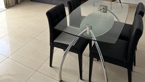 Un salon moderne avec une table à manger en verre, des chaises noires, un canapé gris, un fauteuil marron et un luminaire suspendu au plafond.