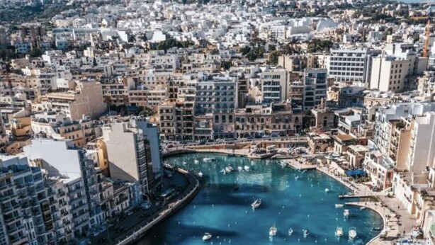 Un paysage urbain côtier avec un port de plaisance rempli de bateaux, entouré de bâtiments très rapprochés les uns des autres.