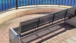 Une promenade en bord de mer avec un banc, une église historique et, en arrière-plan, des bâtiments modernes.