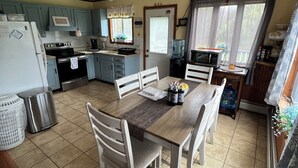 Une cuisine avec des meubles de rangement en bois, une table à manger avec des chaises, un ventilateur de plafond et un distributeur d’eau.