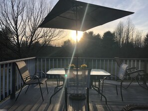 A wooden deck with a table and chairs under a large umbrella, surrounded by a white fence and trees. - Secluded Chalet in the Northern Catskills with FIBER Internet and EV hookup (Summit)