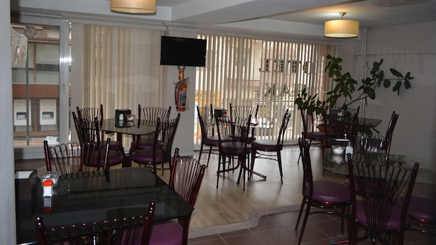 A dining area with a glass table and chairs, a flat-screen TV mounted on the wall, and a fire extinguisher on the wall. - Hak Otel (Merzifon)