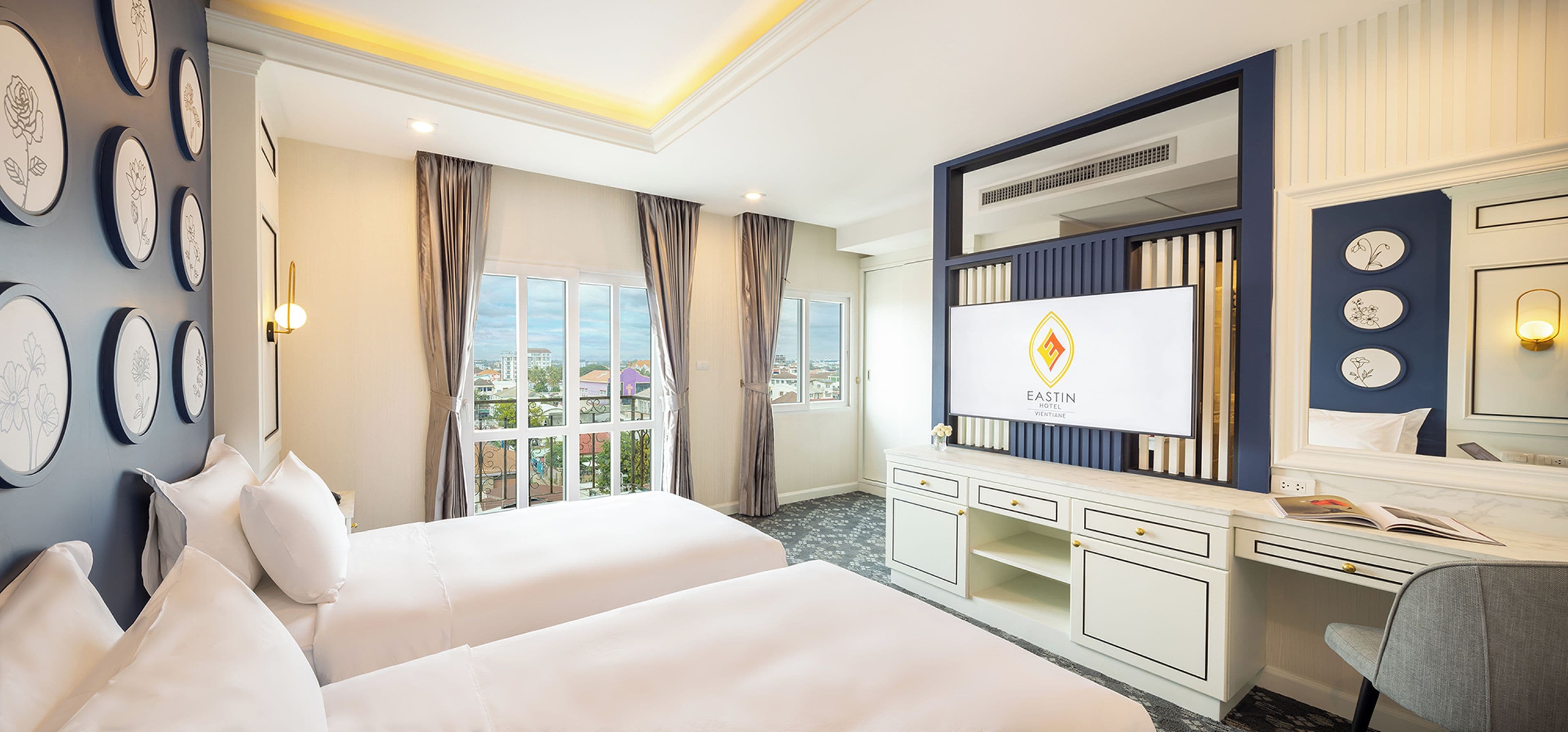 Habitación de hotel con dos camas, un escritorio, una tocador con espejo y vistas a la ciudad.