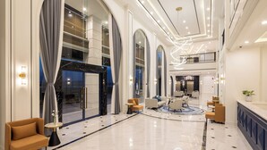 Un amplio vestíbulo con suelo de mármol, ventanas arqueadas grandes y lámparas de diseño moderno.