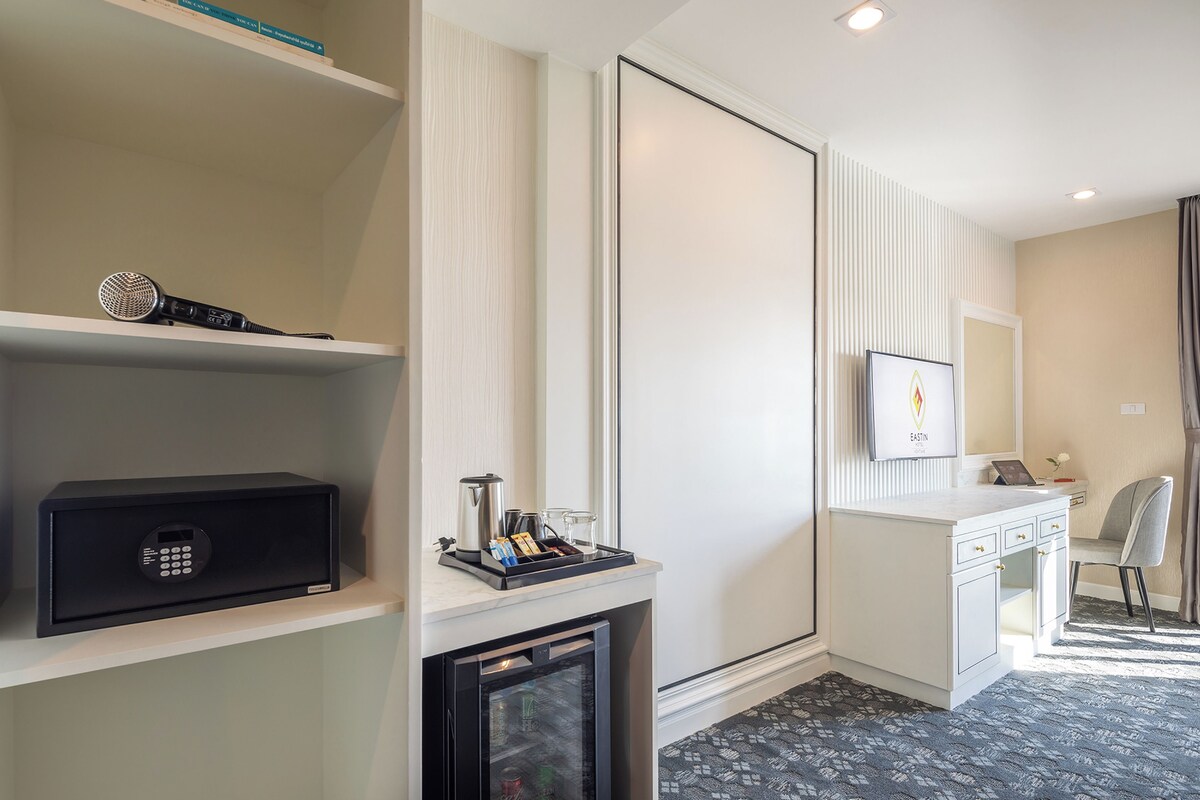 A hotel room with a minibar, a desk with a chair, a television, and a large mirror.