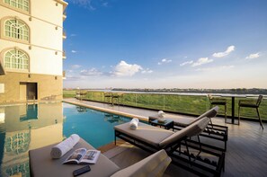 Zona junto a la piscina con sillones, una mesa y un libro, con vistas a un cuerpo de agua y un horizonte urbano distante.