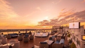 A rooftop bar with outdoor seating and a view of the sunset over a body of water. - Eastin Hotel Vientiane Laos (Vientiane)
