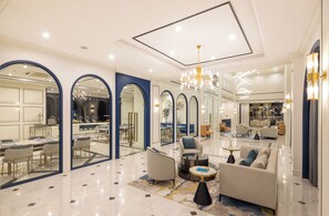 A spacious living area with a modern chandelier, comfortable seating, and a dining area with a glass partition. - Eastin Hotel Vientiane Laos (Vientiane)