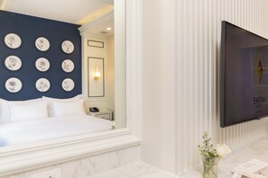 Habitación de hotel con cama, televisión montada en la pared, espejo y pared decorada con motivos florales.
