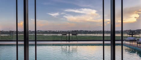 Piscina con dos sillas frente a una vista panorámica de un lago y edificios lejanos al atardecer.