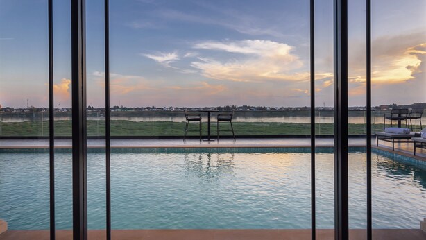 A pool with two chairs facing a scenic view of a lake and distant buildings during sunset. - Eastin Hotel Vientiane Laos (Vientiane)
