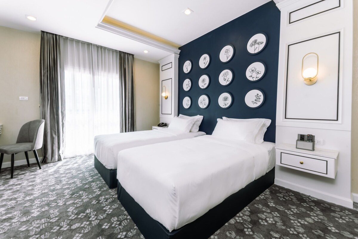 A hotel room with two beds, a desk, a chair, and a wall decorated with circular floral art.