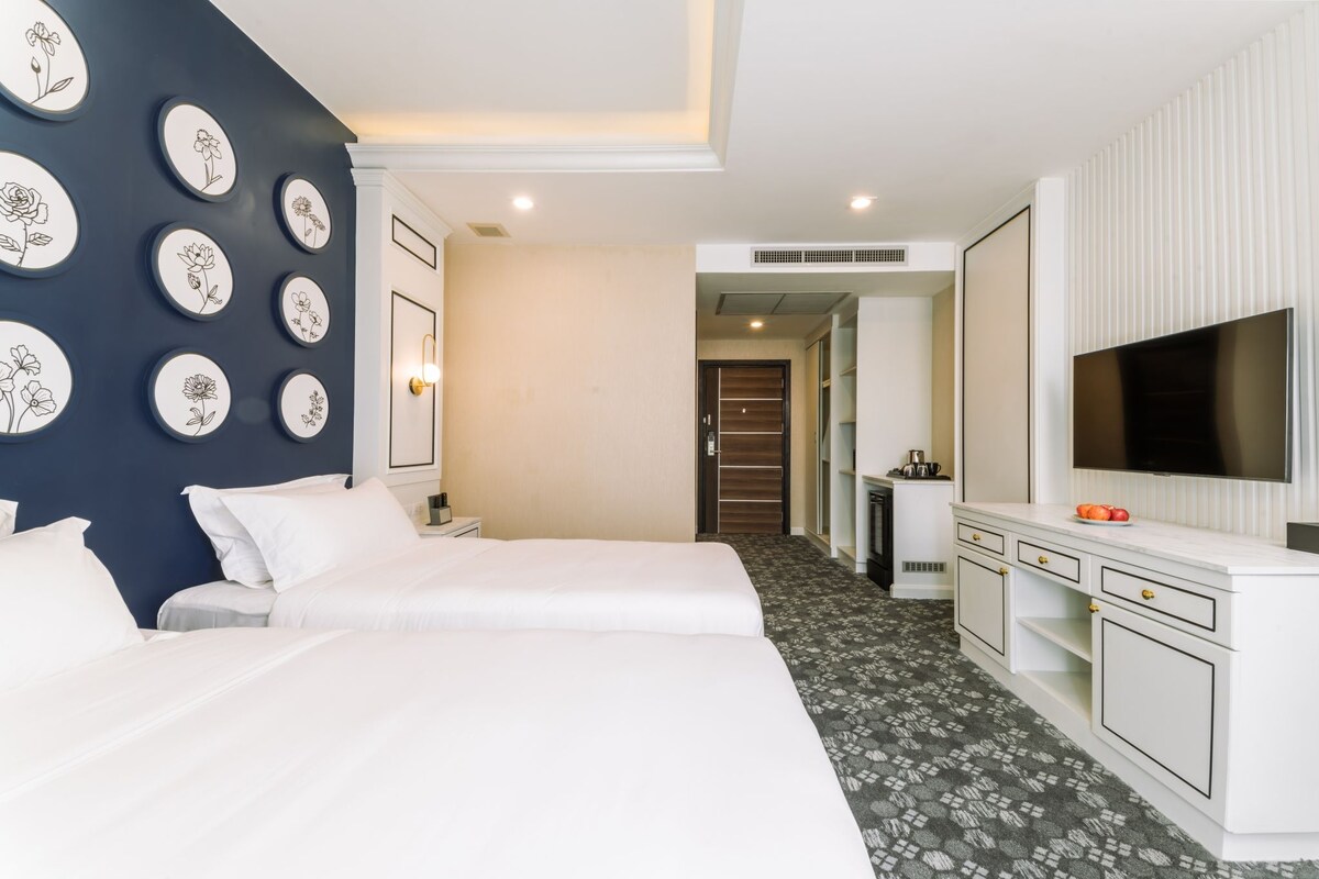 Habitación de hotel con dos camas, televisión, minibar y un diseño floral enmarcado en la pared.