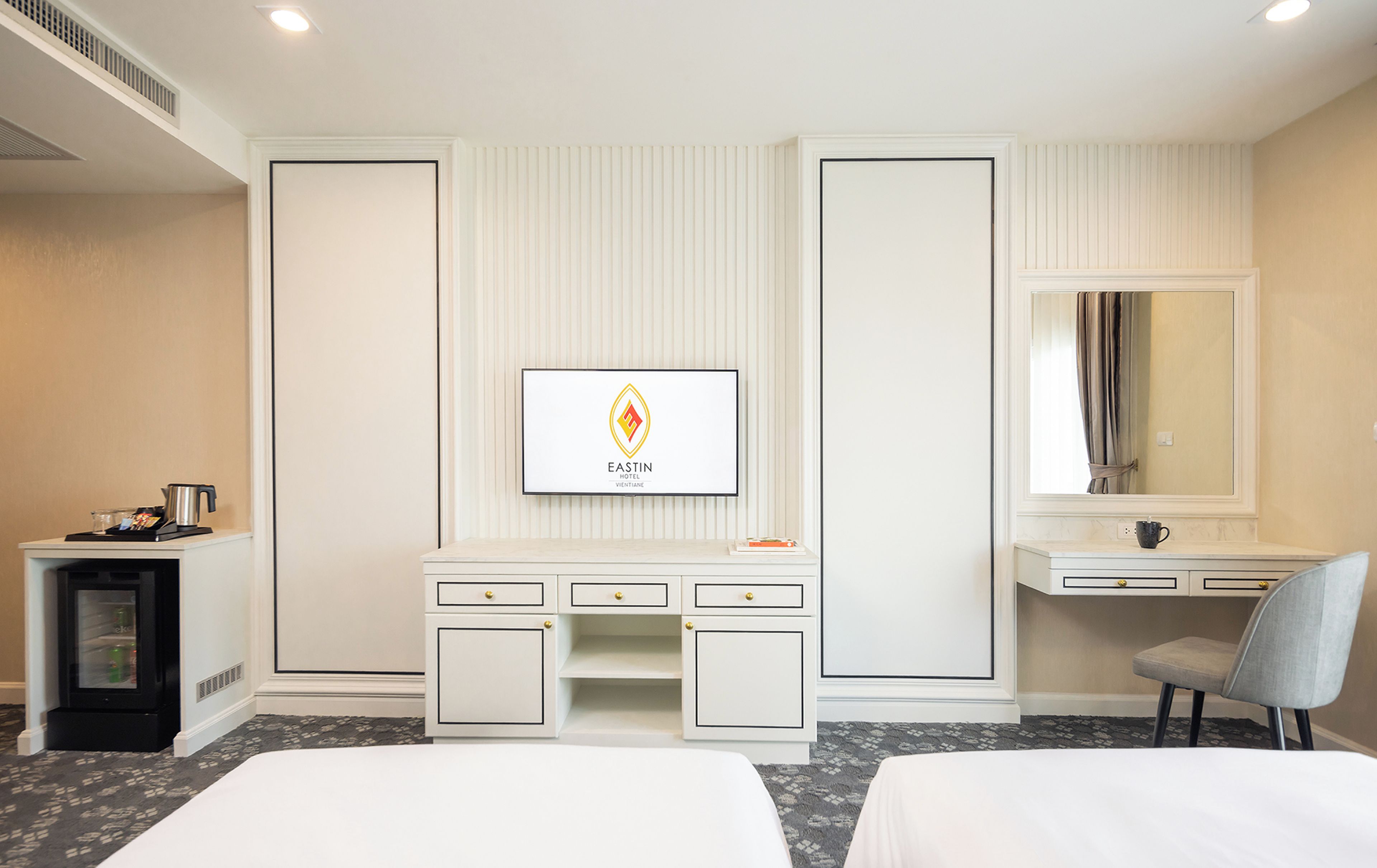 A hotel room with a bed, a desk, a vanity, and a framed logo on the wall.
