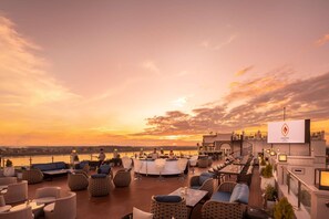 Un bar situat a la terrassa amb seients exteriors i vistes al capvespre sobre una massa d'aigua.