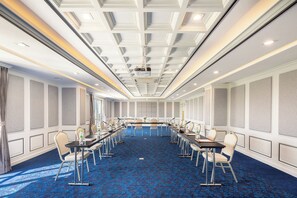 Un salón de conferencias con una larga mesa, sillas y un proyector.