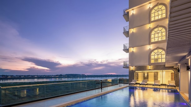 A rooftop pool with a glass barrier, a view of the city skyline, and a building with multiple balconies and large windows. - Eastin Hotel Vientiane Laos (Vientiane)