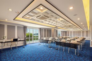A conference room with multiple tables, chairs, and a large window offering a view of greenery. - Eastin Hotel Vientiane Laos (Vientiane)