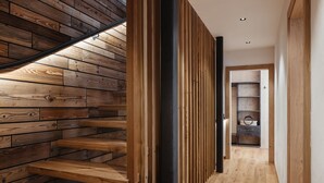 A wooden staircase with a modern design, leading to a hallway with wooden flooring and a built-in shelving unit. - Chalet (LA VALLE)