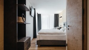 A modern bedroom with a bed, a wooden wardrobe, a shelf with a woven basket, and a TV mounted on the wall. - Chalet (LA VALLE)