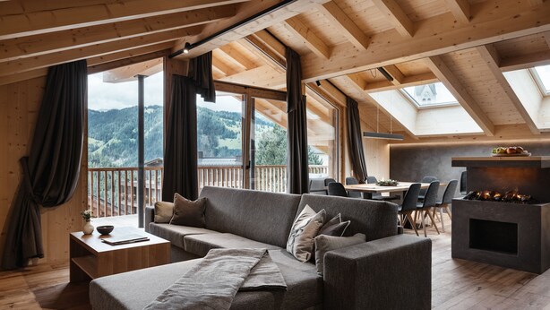 A cozy living room with a sofa, a coffee table, and a fireplace. Large windows offer a view of the outdoors. - Chalet (LA VALLE)
