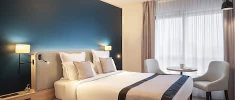 A modern hotel room with a large bed, bedside lamps, a small table, and two chairs.