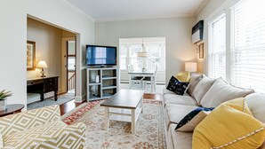 Ein Wohnzimmer mit Sofa, Couchtisch, Fernseher und einem Essbereich mit Tisch und Stühlen.