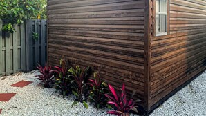A wooden cabin with a window, surrounded by gravel and plants. - Miramar Breeze (Miramar)