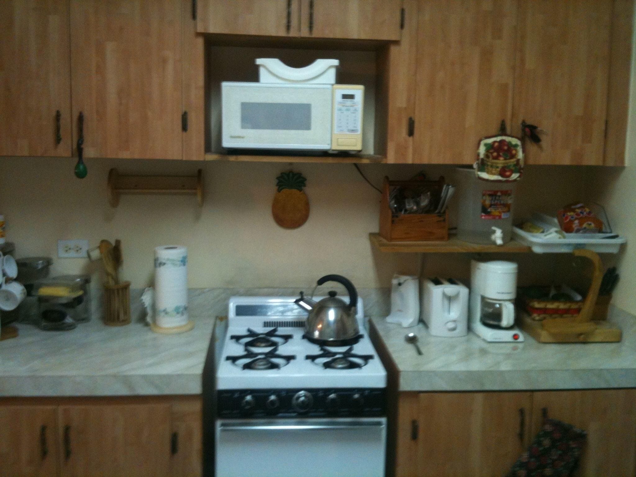 A kitchen with wooden cabinets, a stove, a microwave, and various kitchen items on the counter.
