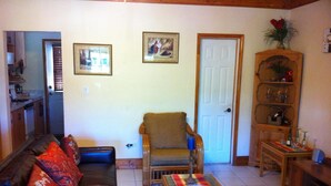 A living room with a sofa, armchair, coffee table, and a wooden cabinet with glassware. - Tangerine Sunsets Tangelo (Nassau)