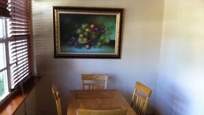 A dining area with a wooden table and chairs, a painting on the wall, and a window with blinds. - Tangerine Sunsets Tangelo (Nassau)