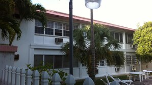 A building with a white facade, multiple windows, and a red roof. There are palm trees and a white picket fence in the foreground. - Tangerine Sunsets Tangelo (Nassau)