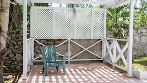 Un patio couvert avec une seule chaise verte et une cloison en treillis blanc.