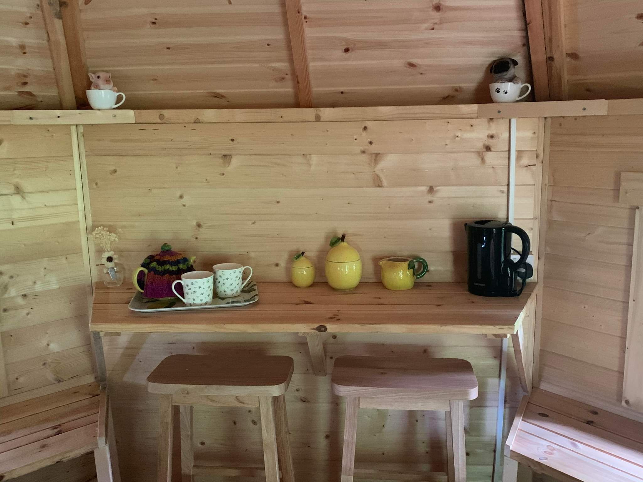 Un interior de madera con un banco, una bandeja con tazas, una tetera y una cafetera.