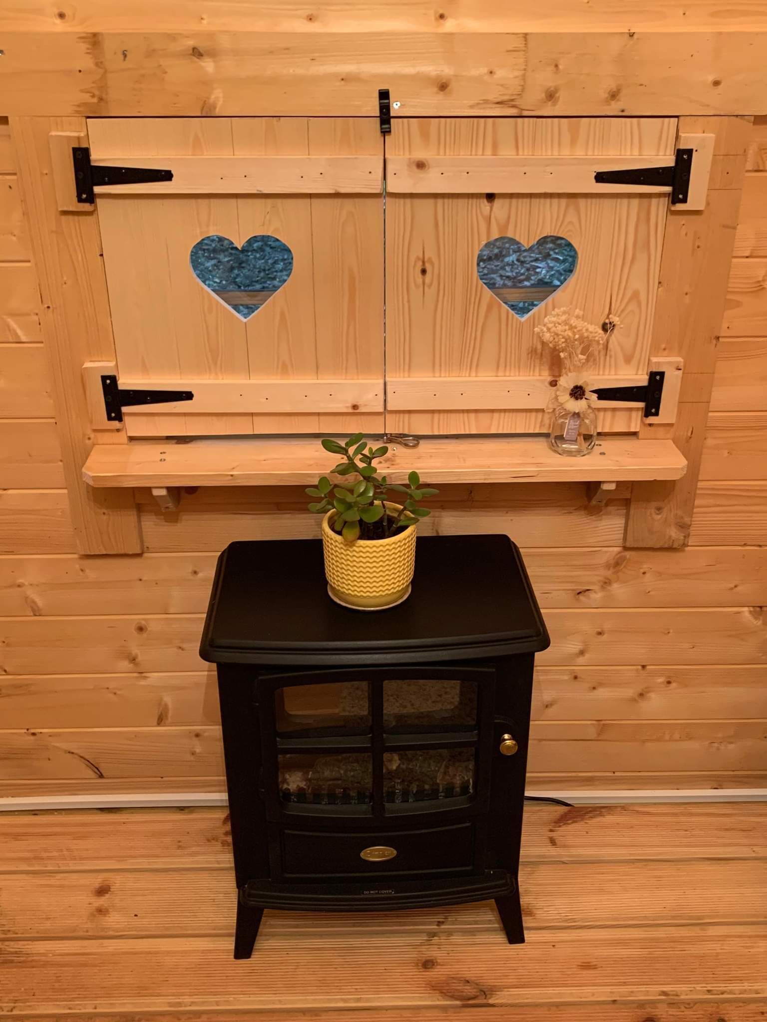 Una habitación de madera con una estufa negra, una estantería con una planta y decoraciones con forma de corazón en la pared.