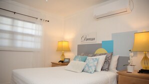 A neatly arranged bedroom with a large bed, two bedside tables, and a wall-mounted air conditioner. - Tangerine Sunsets Fairchild (Nassau)
