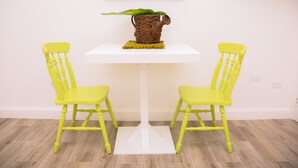Taula petita blanca amb un suport trenat per plantes i una placemat groga. Dues cadires grogues estan col·locades a cada banda de la taula.