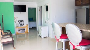 Une cuisine moderne avec des meubles blancs, un réfrigérateur en acier inoxydable et un coin repas comprenant deux chaises blanches et des coussins rouges.