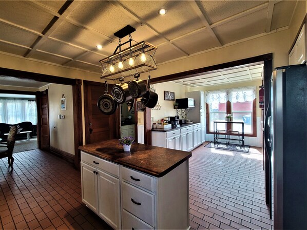 A kitchen with white cabinets, a brown countertop, hanging pots, and a ceiling light fixture. - Charming Farmhouse in the Orchards near Lake Mich! (New Era)