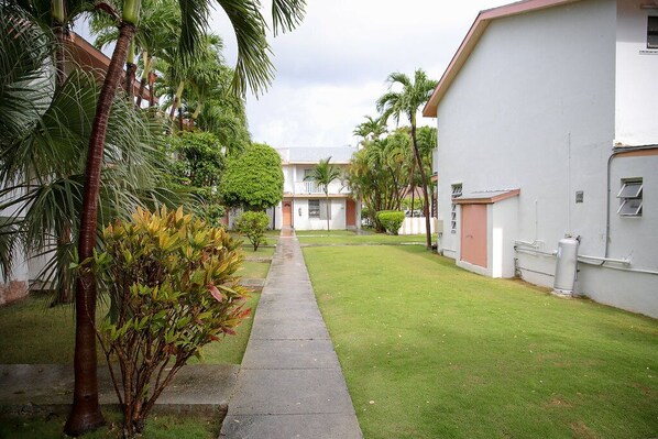 A courtyard with a pathway leading to a building with a white exterior and a red door. - Tangerine Sunsets Fallglo (Nassau)
