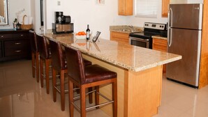 A kitchen with wooden cabinets, a stainless steel refrigerator, a granite countertop, and a ceiling fan. - Tangerine Sunsets Satsuma One (Nassau)