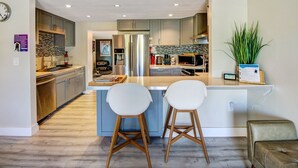 Una cocina moderna con una isla central, electrodomésticos de acero inoxidable y taburetes de bar de madera.