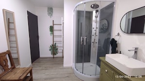 A bathroom with a glass-enclosed shower, a wooden bench, a white sink, and a mirror.