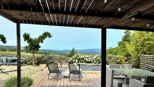 A wooden deck with outdoor furniture, a hammock, and a view of the landscape.