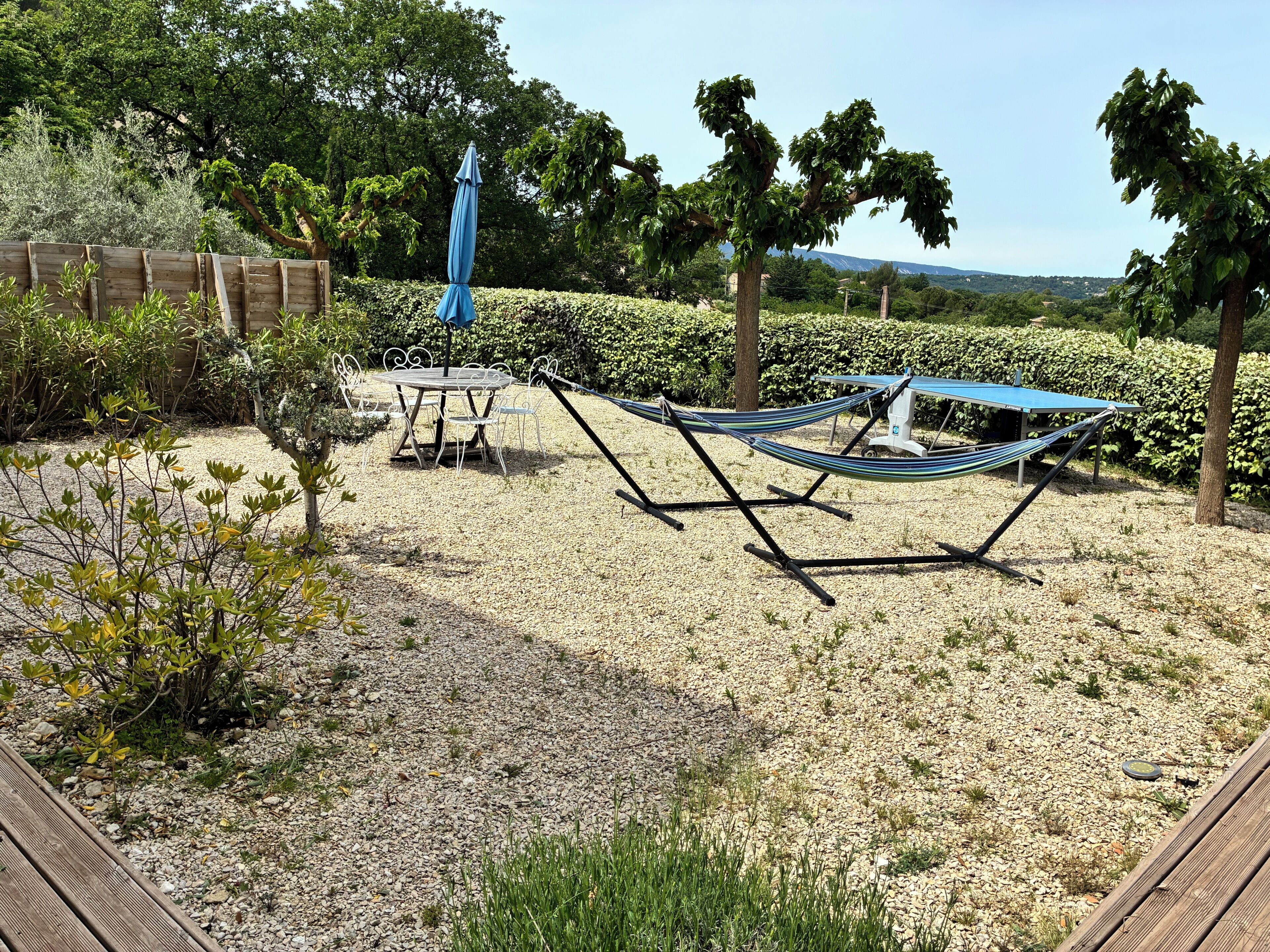 Un jardin avec un hamac, une table et des chaises, et un parasol bleu.