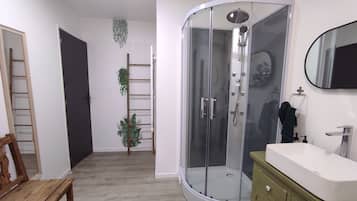 Een badkamer met een douchecabine van glas, een houten bankje, een wit wastafelmeubel en een spiegel.